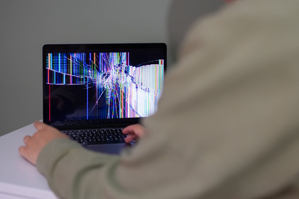 A person interacts with a laptop that has a cracked and distorted screen.