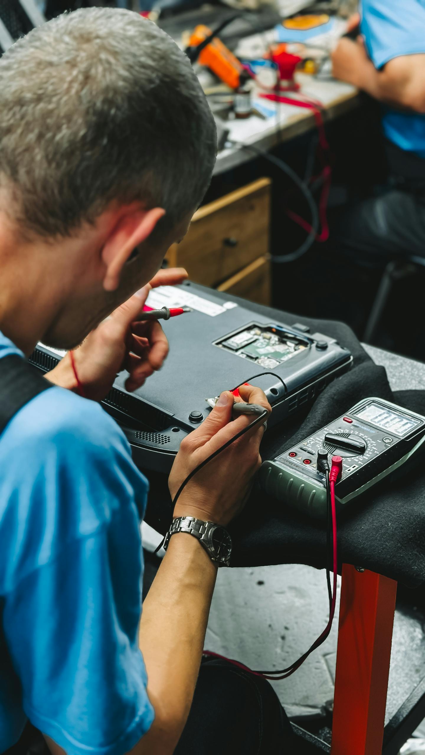 Professional technician repairing an electronic device with precision tools and a multimeter.
